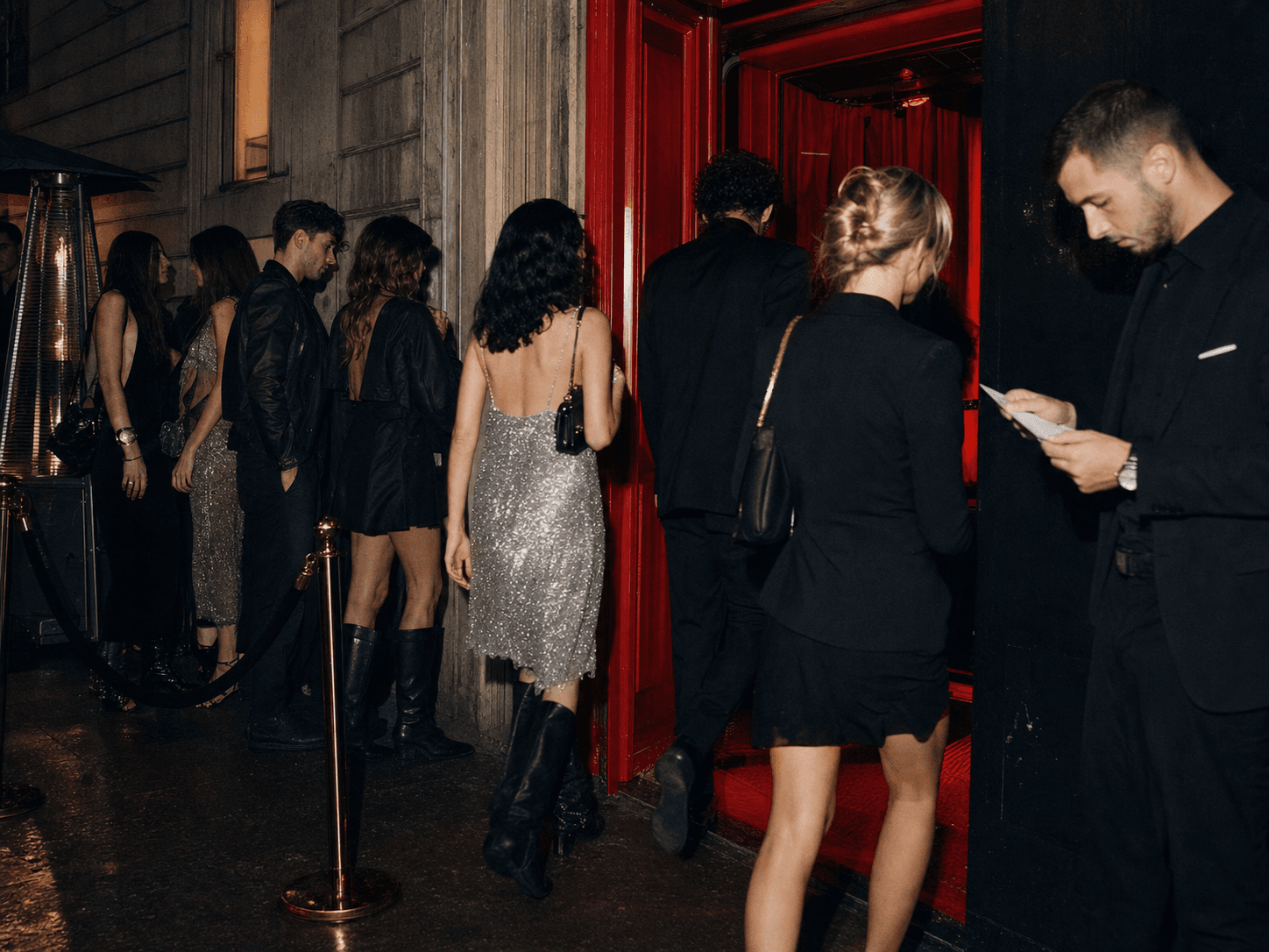 Stylish guests entering a red doorway late at night